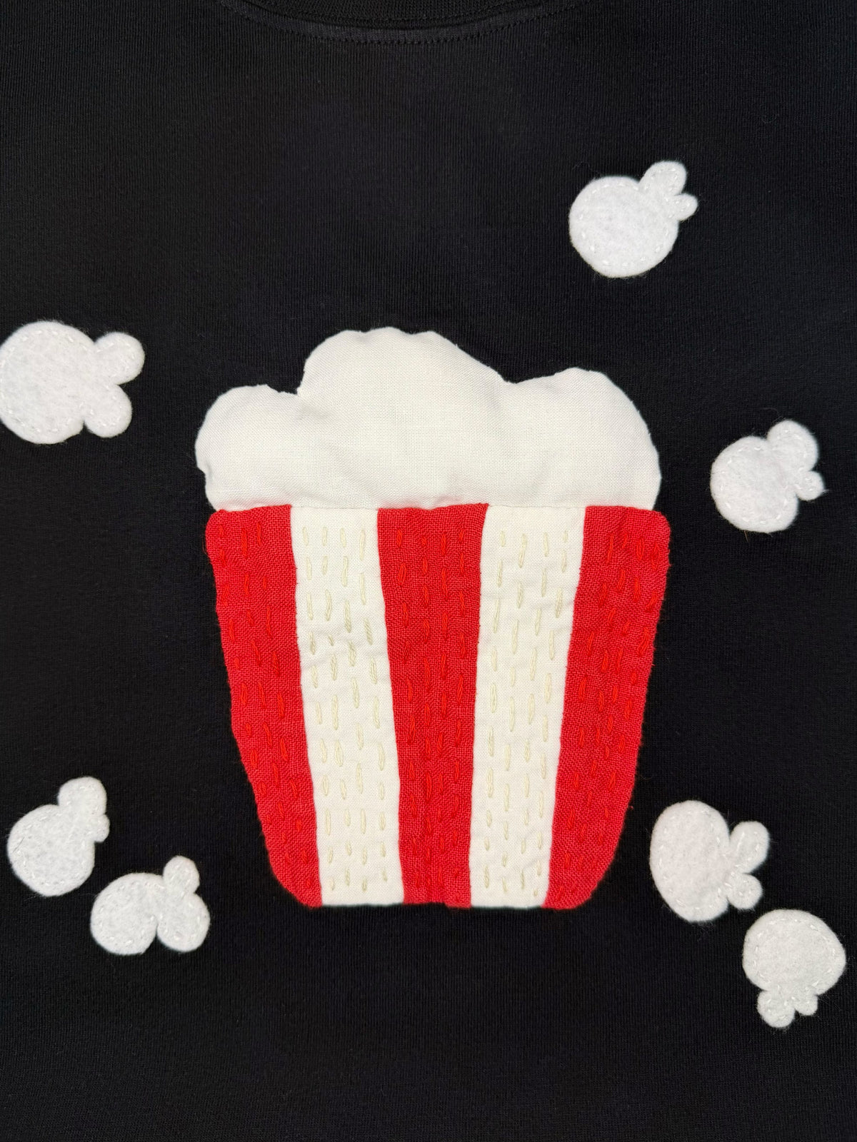 Close up shot of a black t-shirt with a red and white popcorn appliqué design