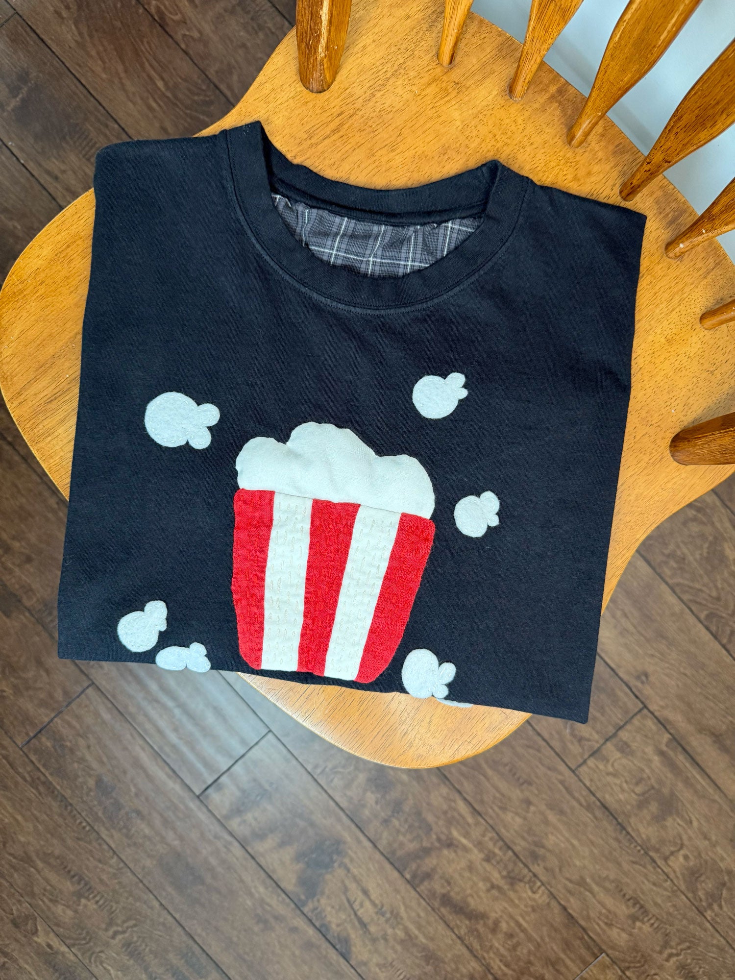 Black t-shirt with a popcorn appliqué design folded on wooden chair