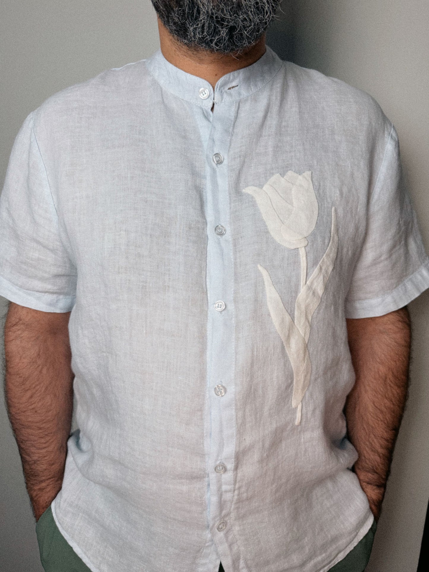 Person wearing a light blue linen shirt with a off white tulip design against a neutral background