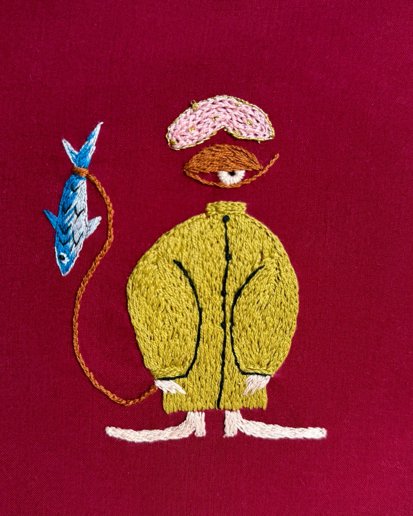 Embroidery of a character with a blue fish on a red fabric.
