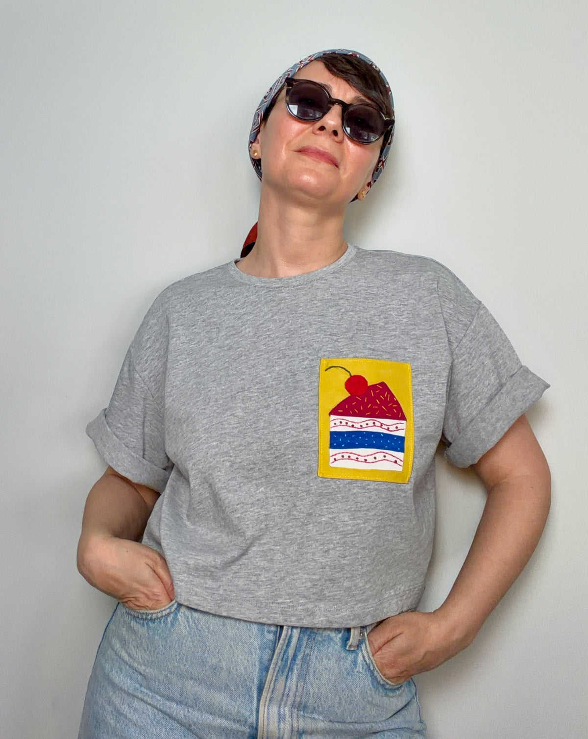 Person wearing a grey t-shirt with a colourful hand appliqué graphic design stitched on a plain yellow fabric patch.