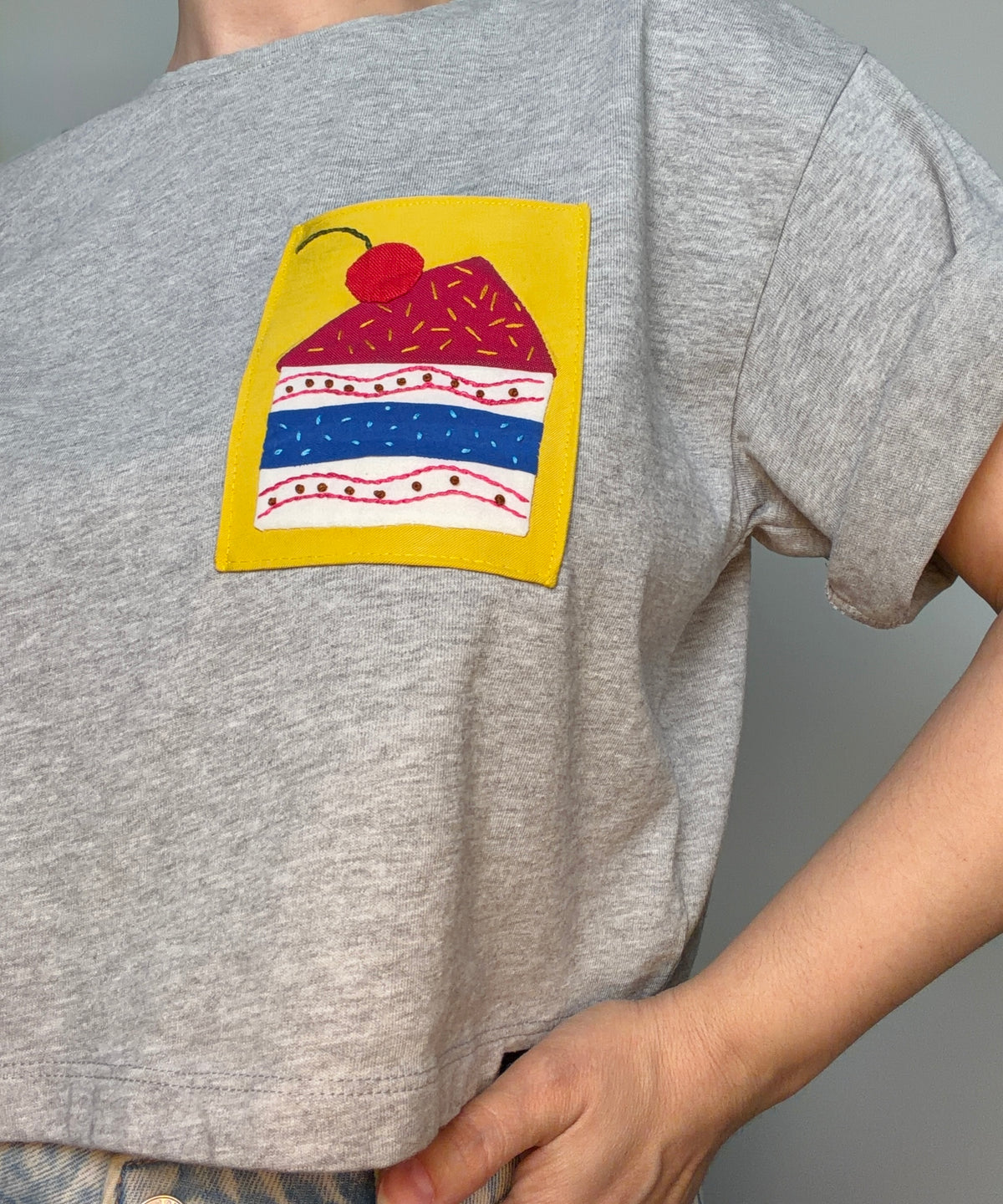 A grey t-shirt with a colourful hand appliqué graphic on a yellow background fabric patch.