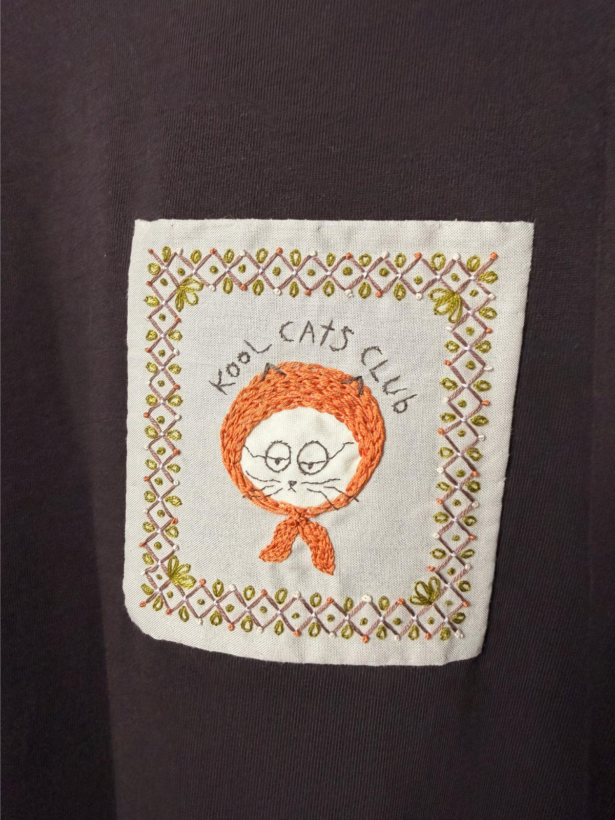 Embroidered patch with a cat design and 'Kool Cats Club' text on a dark purple cotton t-shirt.